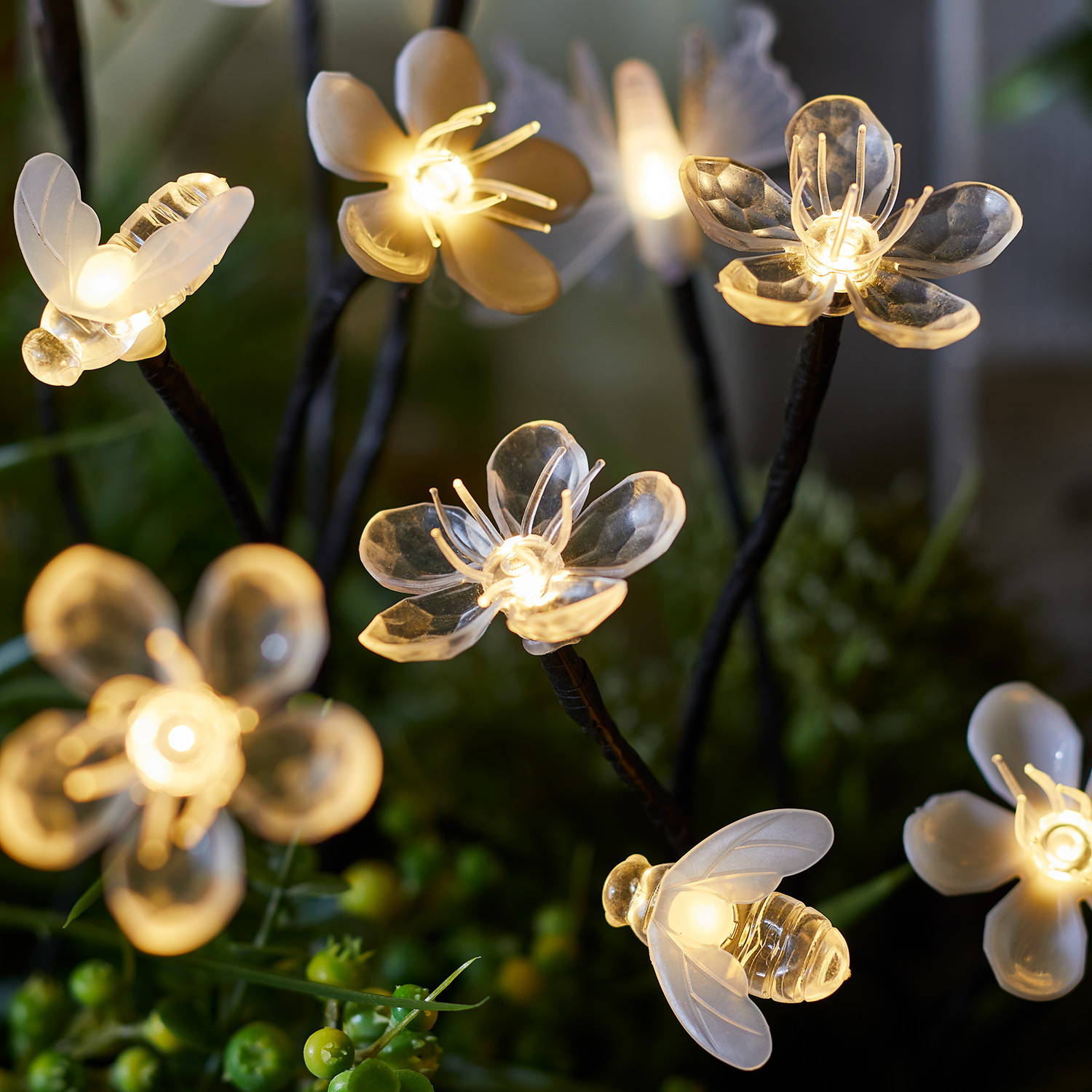 Flower, bee and butterfly solar stake lights illuminated in greenery