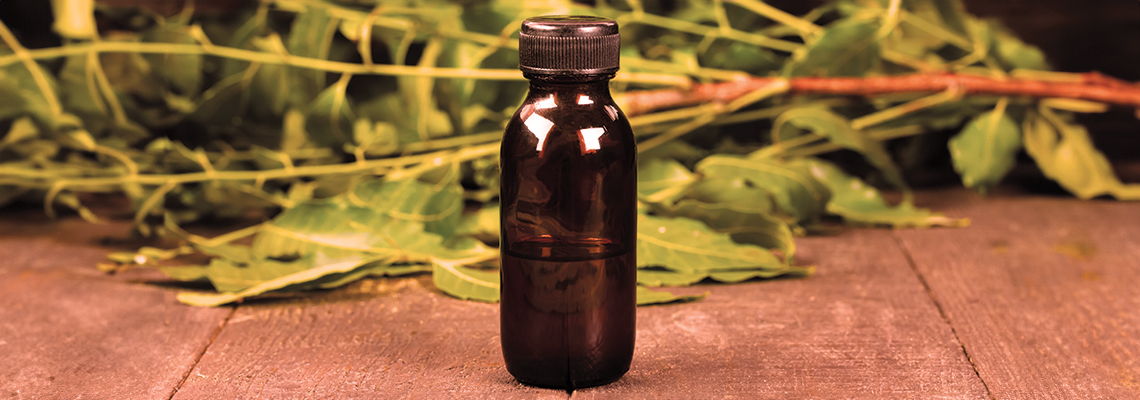 Brown glass bottle on a wooden surface with green leaves in the background.