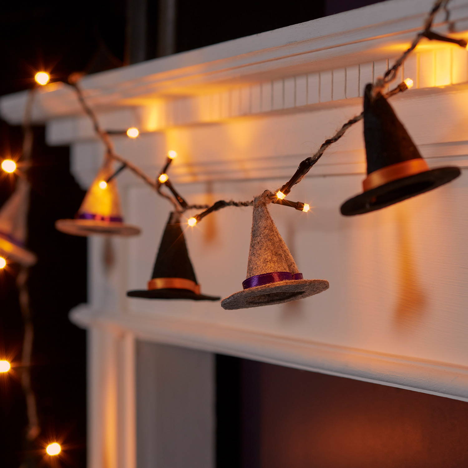 Black and grey witches hat fairy lights draped across a white mantelpiece. 
