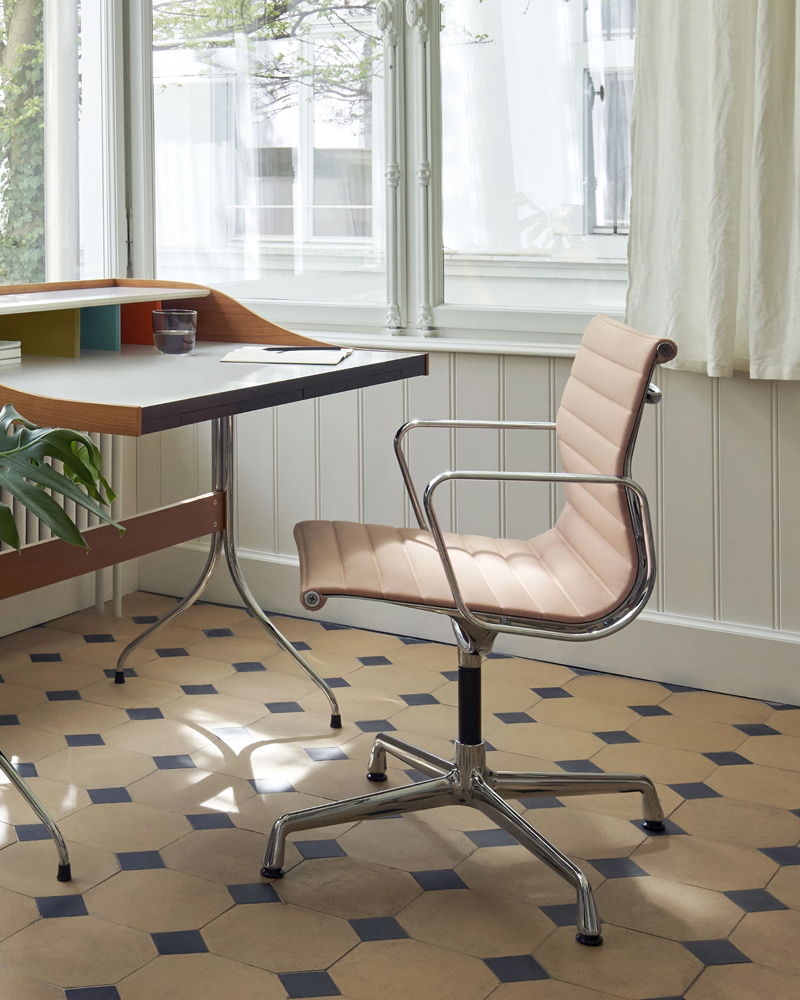 A modern Eames Aluminium desk chair next to a desk in a well-lit room.