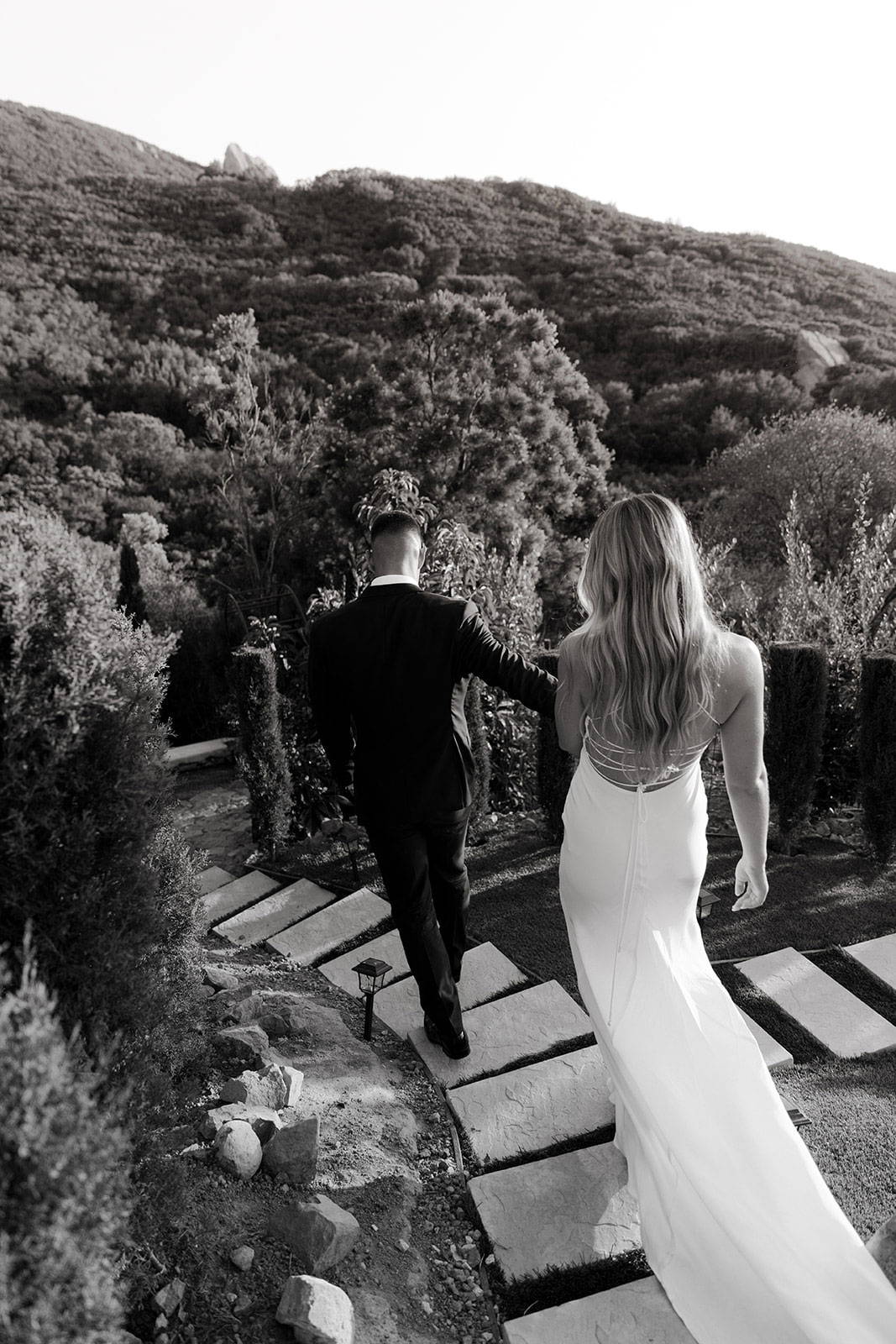 Image en noir et blanc de la mariée et du marié descendant les marches d'une colline