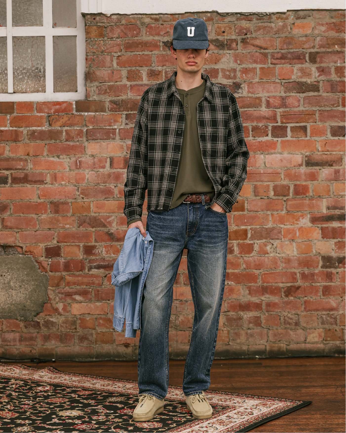 Person standing in front of a brick wall, wearing casual clothing and a cap.