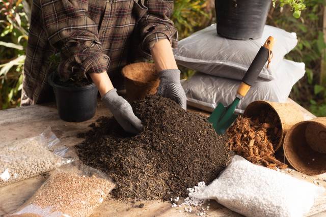 A person mixes potting soil ingredients preparing to plant container garden