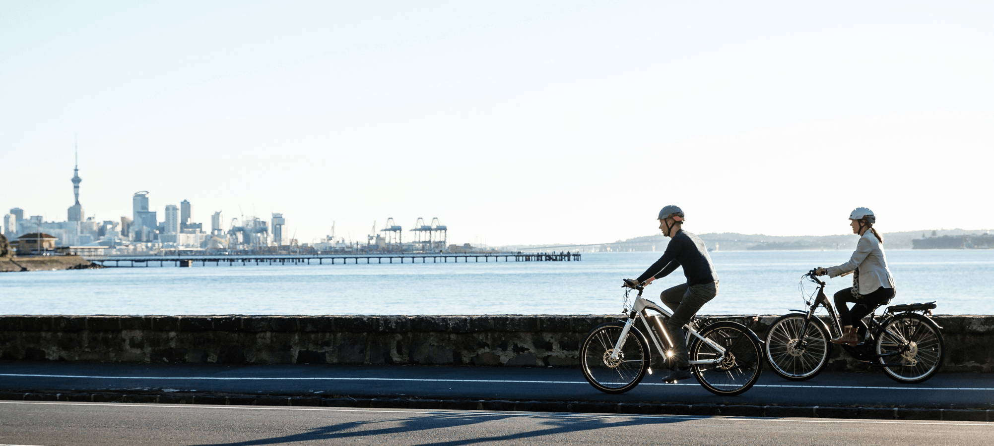 couple riding their smartmotion ebikes in Auckland New Zealand with the city background and the sea