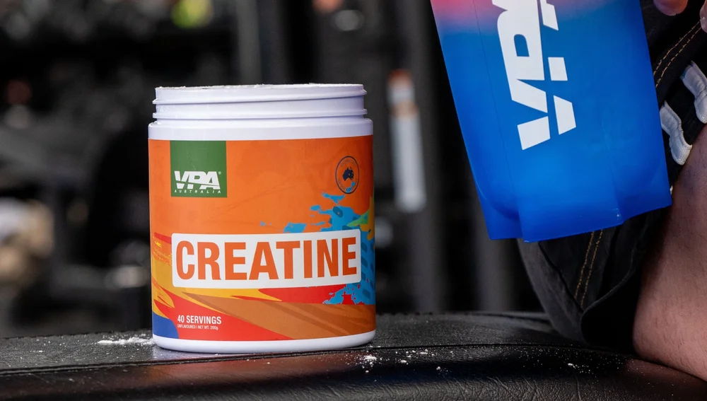Container of creatine supplement next to a blue shaker bottle.