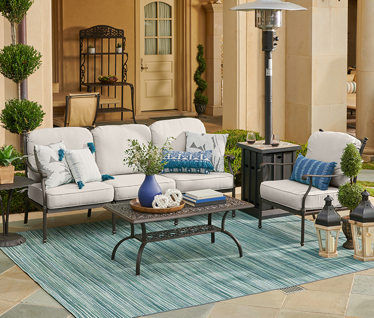 Outdoor seating area with cushions, table, and decorative plants.