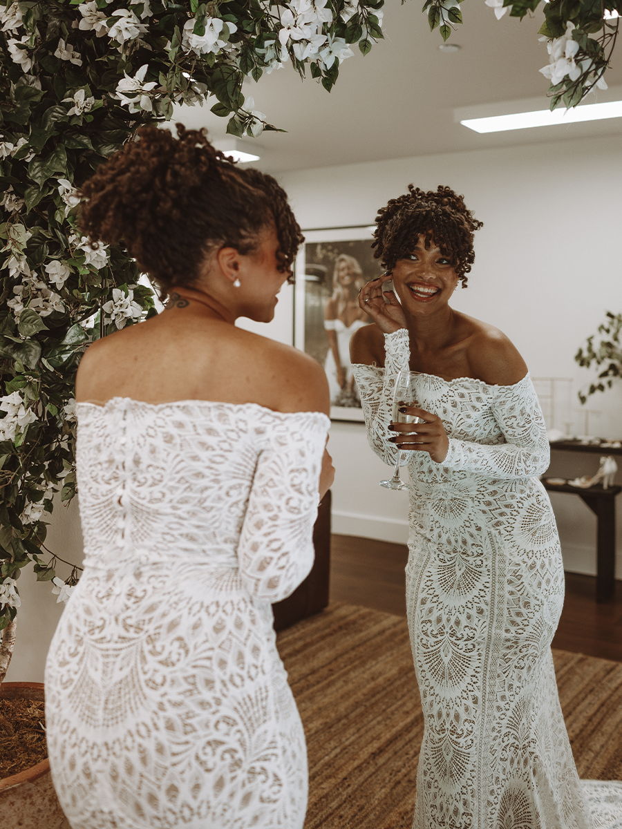 Two women in elegant dresses admiring themselves in a mirror.