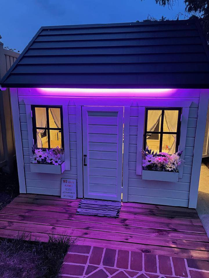 Illuminated Kids Playhouse with white flower boxes and terrace in the backyard by WholeWoodPlayhouses