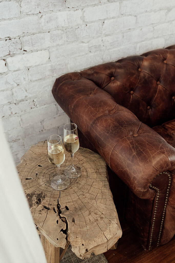 Two champagne glasses on rustic timber table with chocolate leather couch