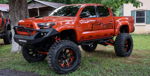 Side profile orange lifted Toyota Tacoma HORNBLASTERS decals HULK grille Nitto Trail Grappler grass barn Billy's 244K Nightmare Edition featured gallery photo 1
