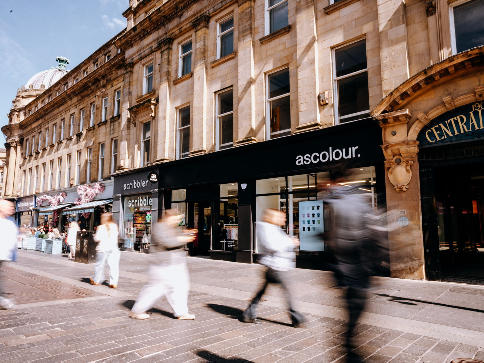 People walking past shops on a busy street.