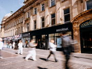 People walking past shops on a busy street.