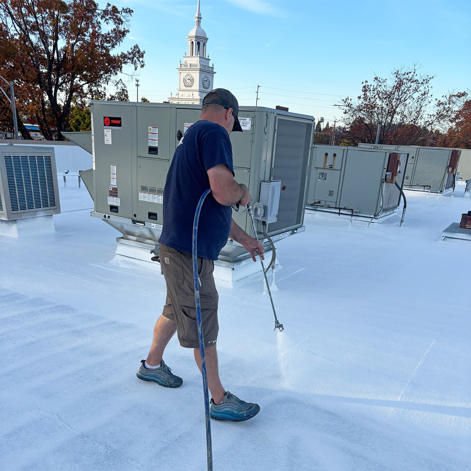 A man spraying foam on a rooftop with HVAC units in the background.