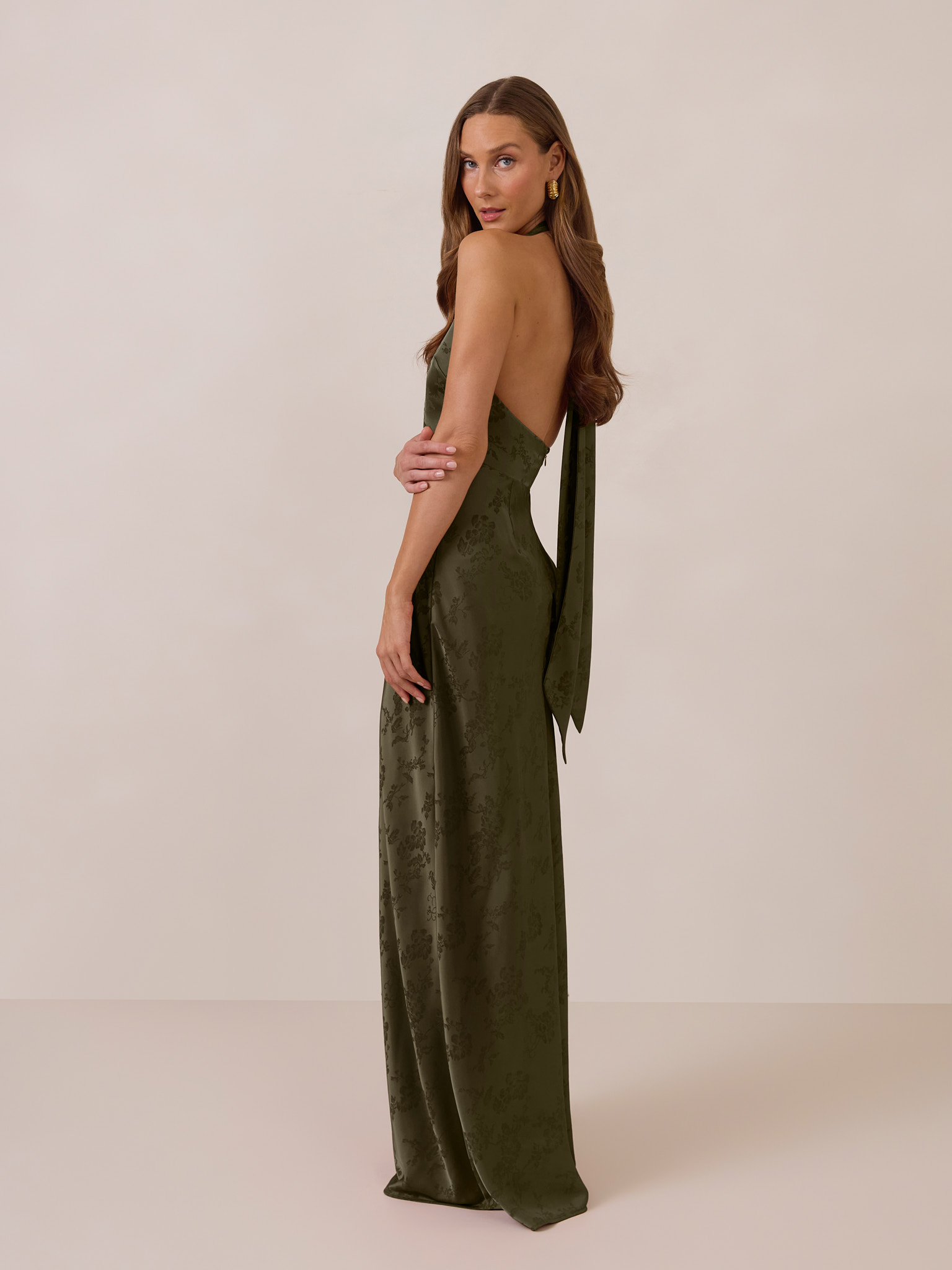 Woman in a long, olive green dress standing against a neutral background.