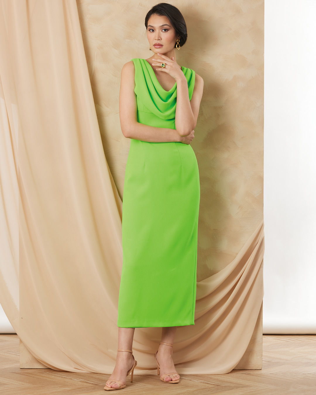 A woman in a green dress poses against a neutral backdrop.