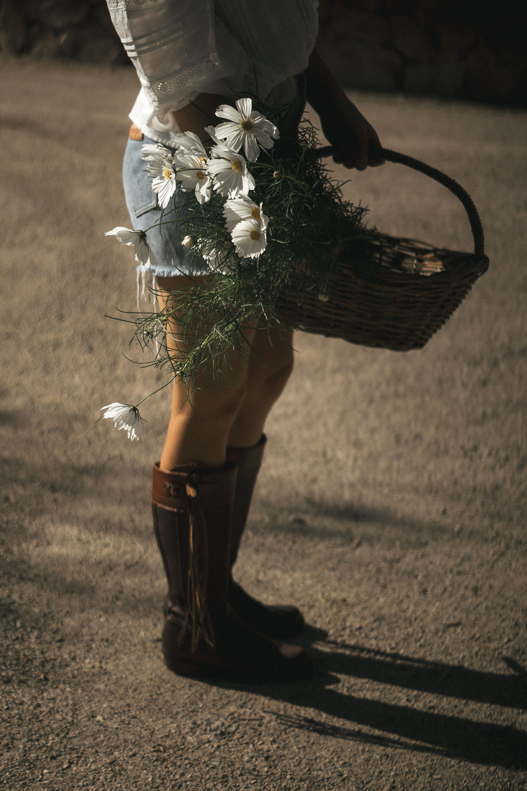 Person holding a basket of flowers, wearing shorts and brown boots.