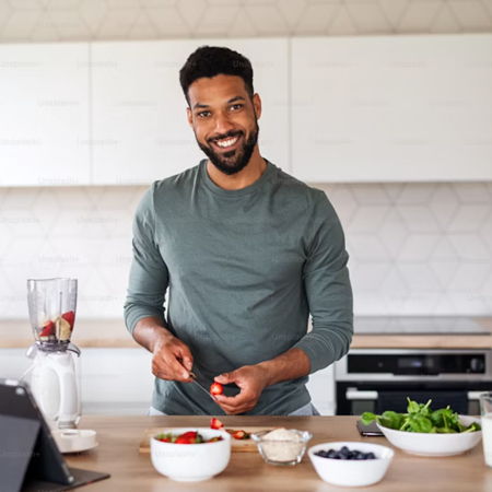 Man preparing food in a kitchen with fruits and vegetables on the counter.