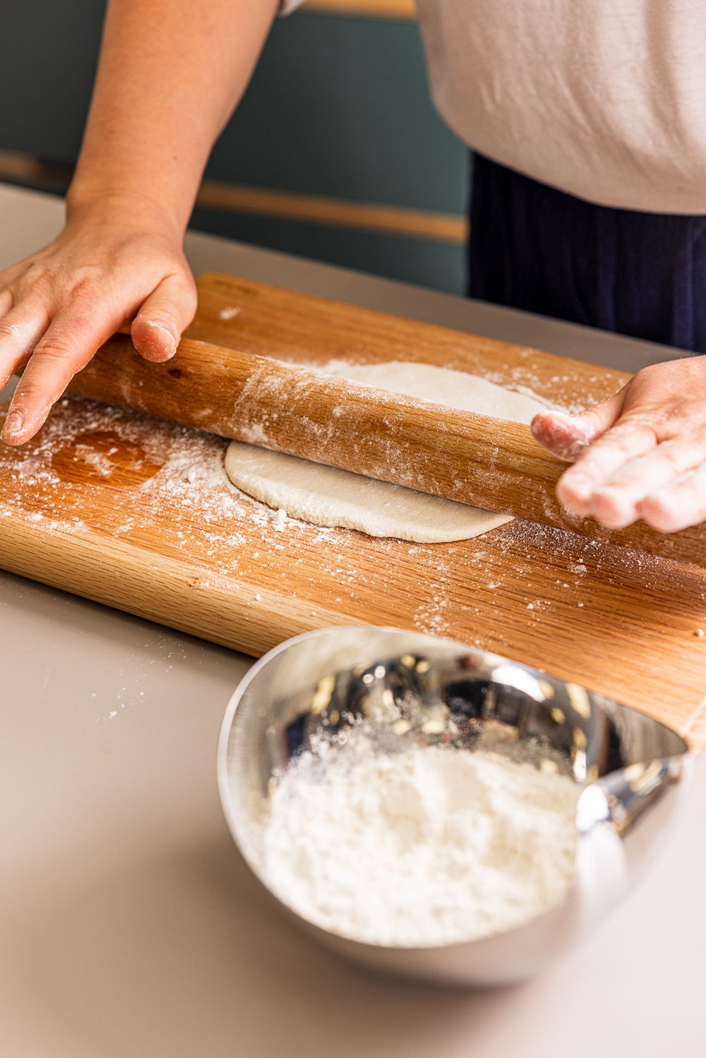 Person rolling dough on a Classic Chopping Board with flour and a Drift Bowl nearby.