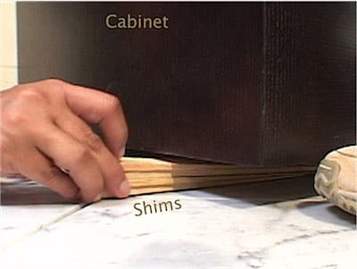 Hand placing shims under a cabinet on a marble surface.