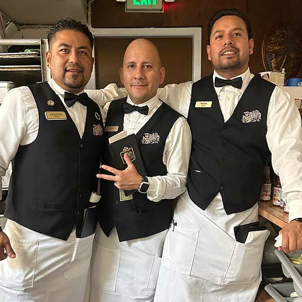 Waiters wearing black bow ties, vests and aprons while working