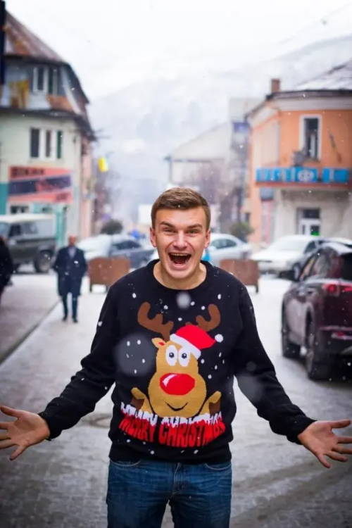 Image of man in snow wearing reindeer Christmas sweater.