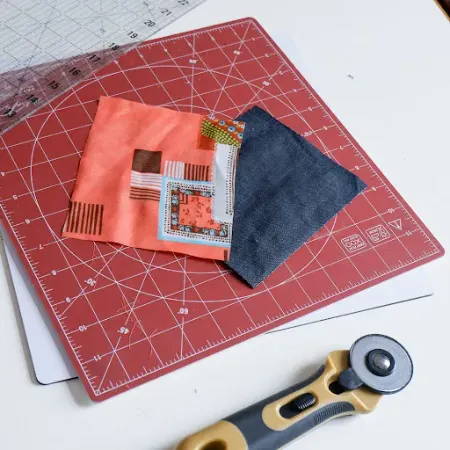Two fabric pieces on a rotating cutting mat with a quilt ruler and a rotary cutter