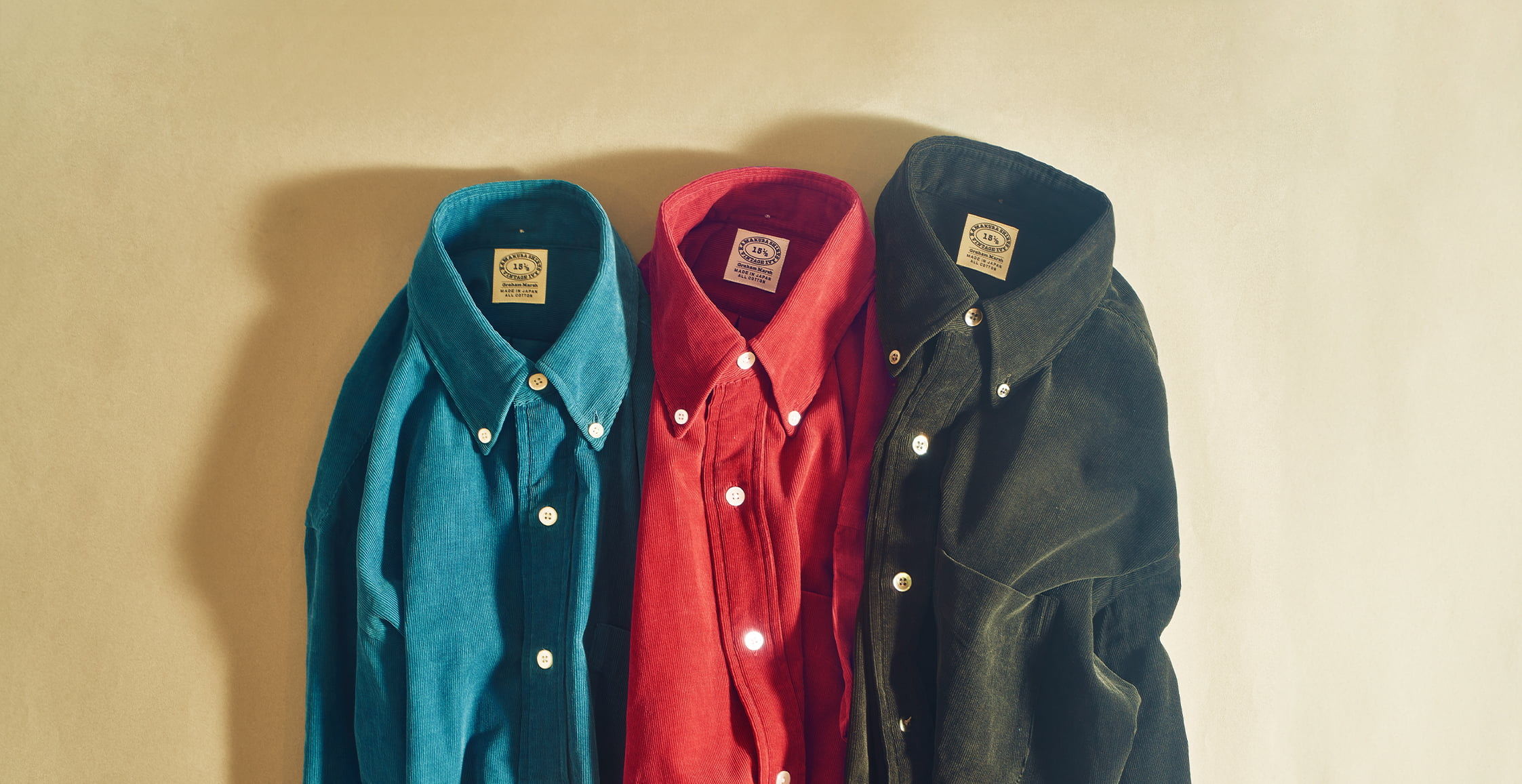 Three collared shirts in teal, red, and black hanging against a wall.