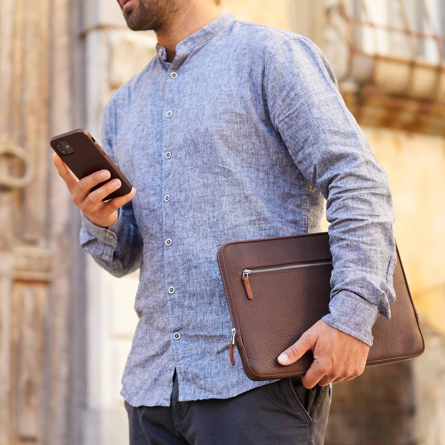 Ein Mann trägt eine Macbook Hülle aus Leder unter dem Arm