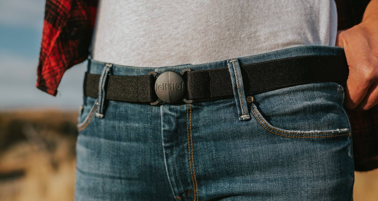 Woman featured wearing Jelt Original elastic stretch belt in black granite. Worn with jeans, white t-shirt and a red flannel shirt.