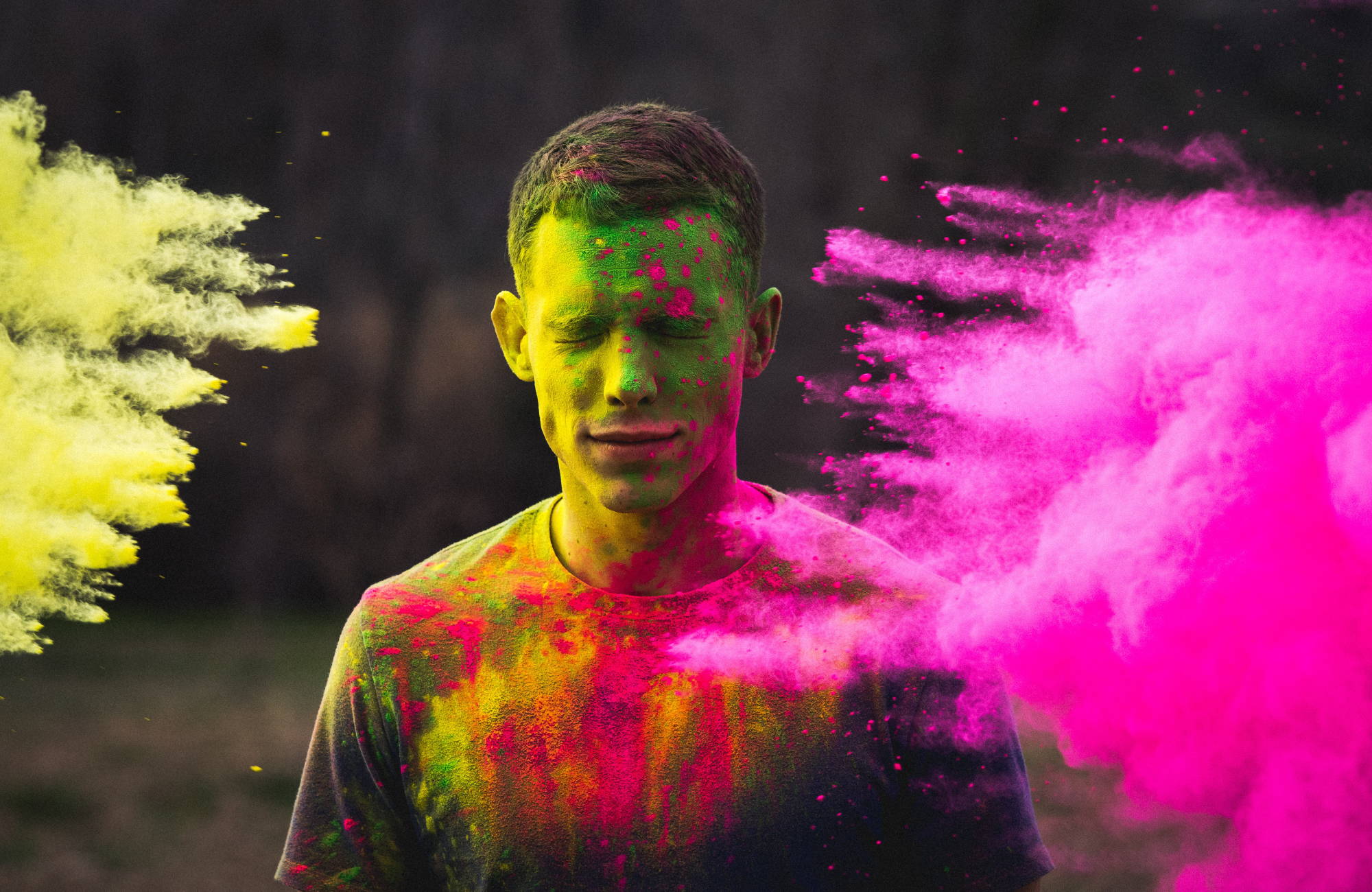  A man covered in green and pink powder stands as green and pink powder comes at him from both sides