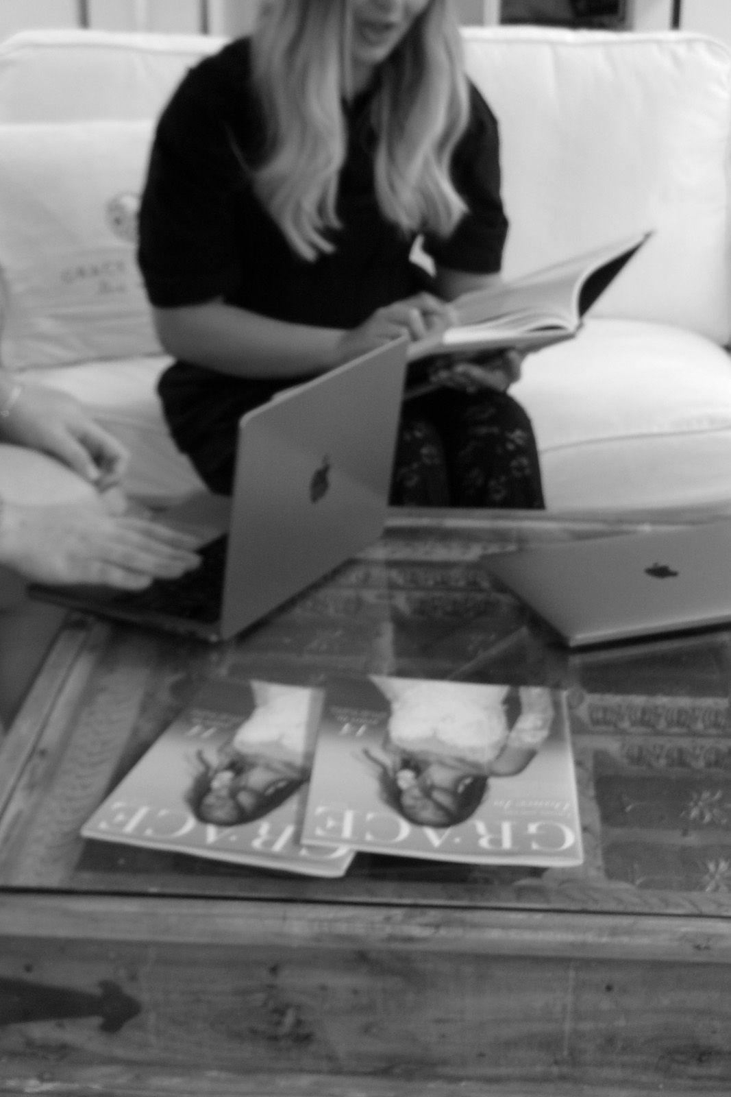 Person reading a book and using a laptop on a coffee table.