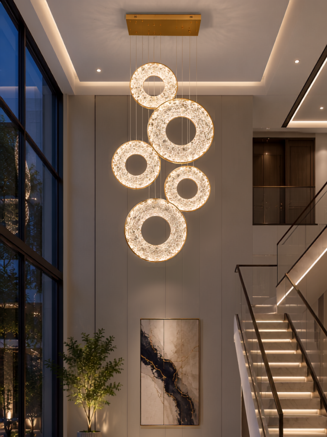 Three crystal rings hung at mid height between two levels in a double- height stairwell beside a straight staircase