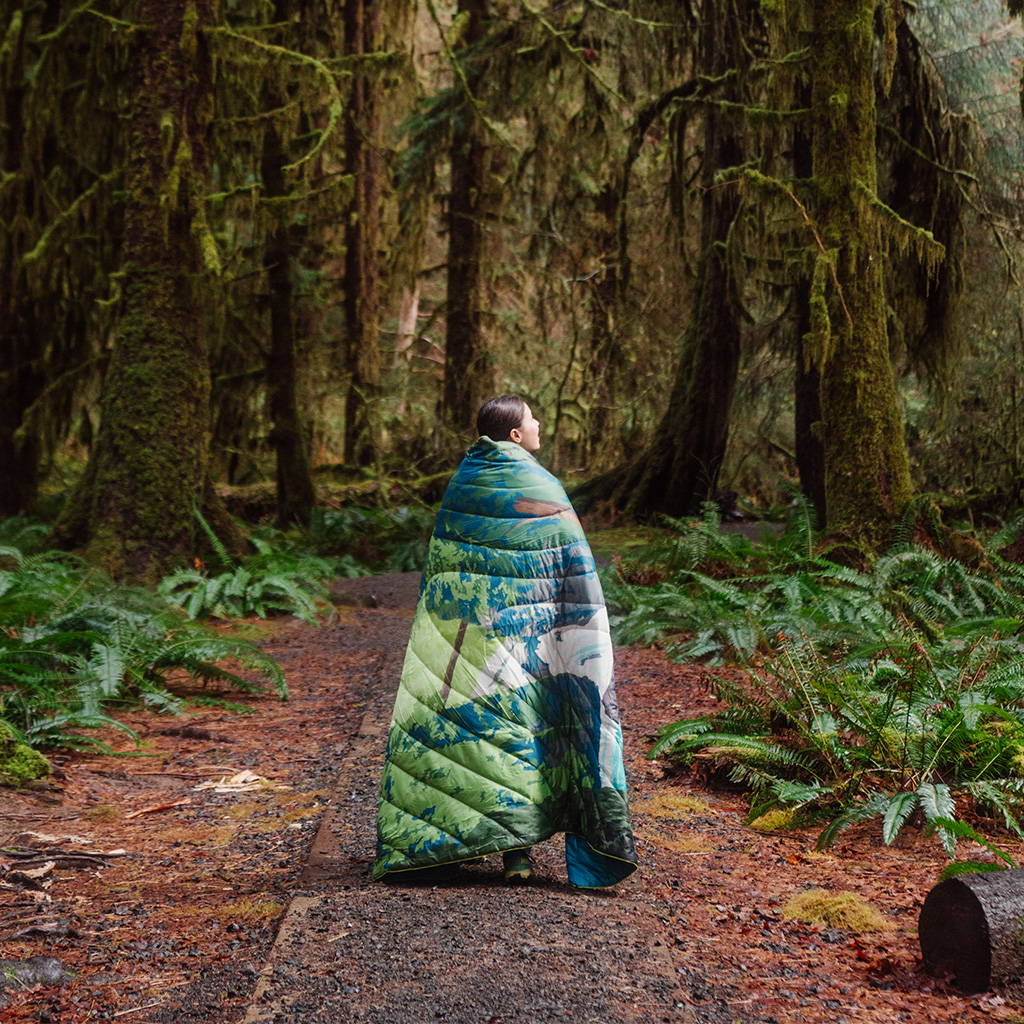 A woman takes an Olympic Nationalk Park Original Puffy Blanket on a walk with her through the 