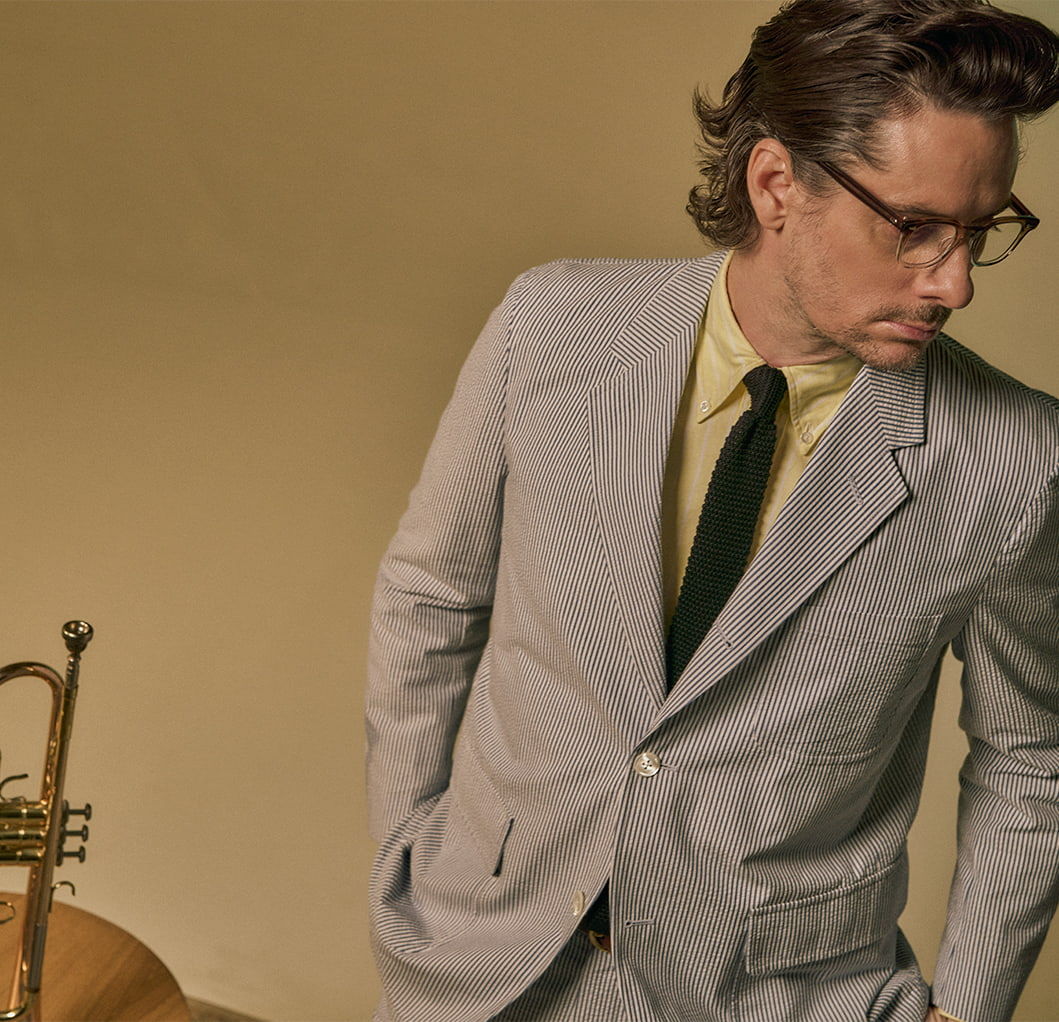 Man in a suit looking down beside a trumpet against a plain background.