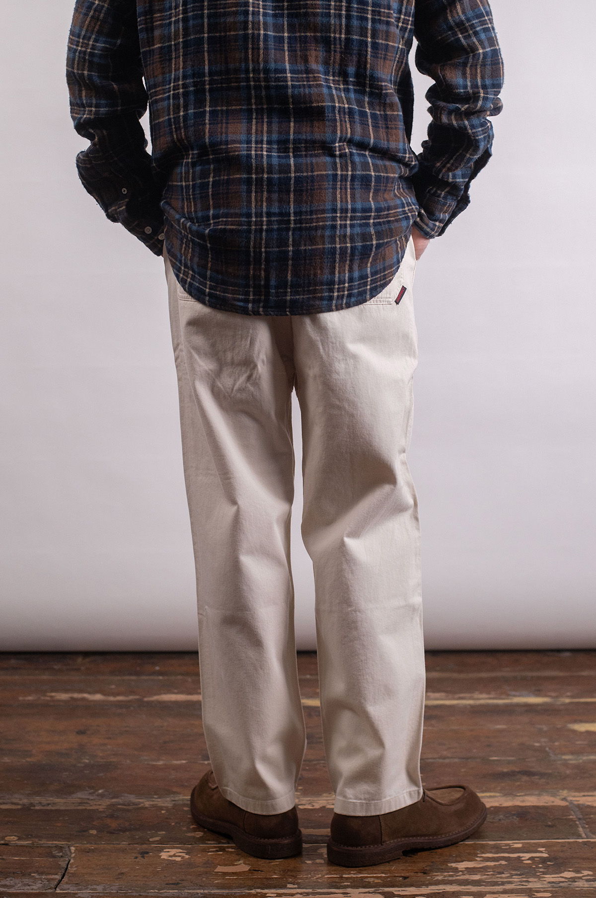 Person wearing a plaid shirt and light-colored pants standing on wooden floor.