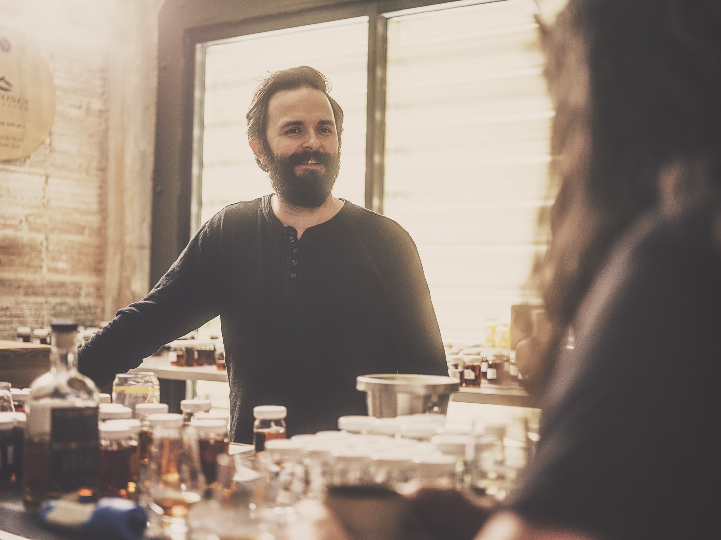 A smiling man in a dark sweater stands behind a counter, engaging in conversation.