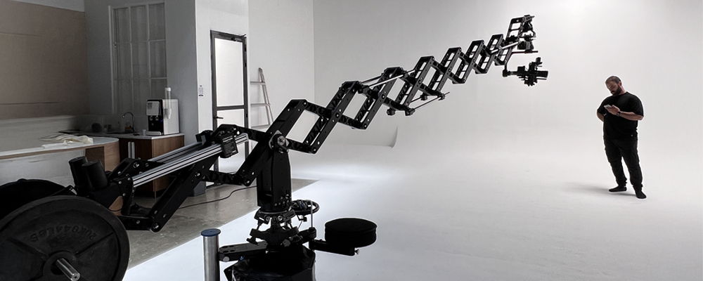 A man stands near a mechanical arm in a studio.