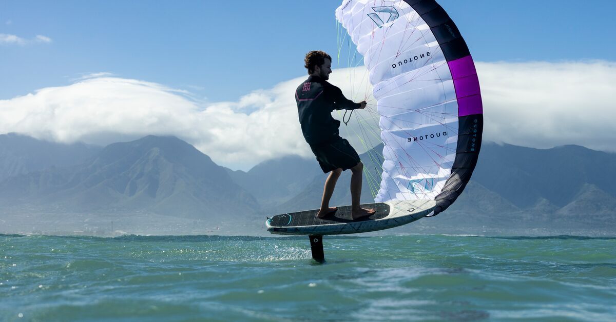 A person kitesurfing on water with mountains in the background.