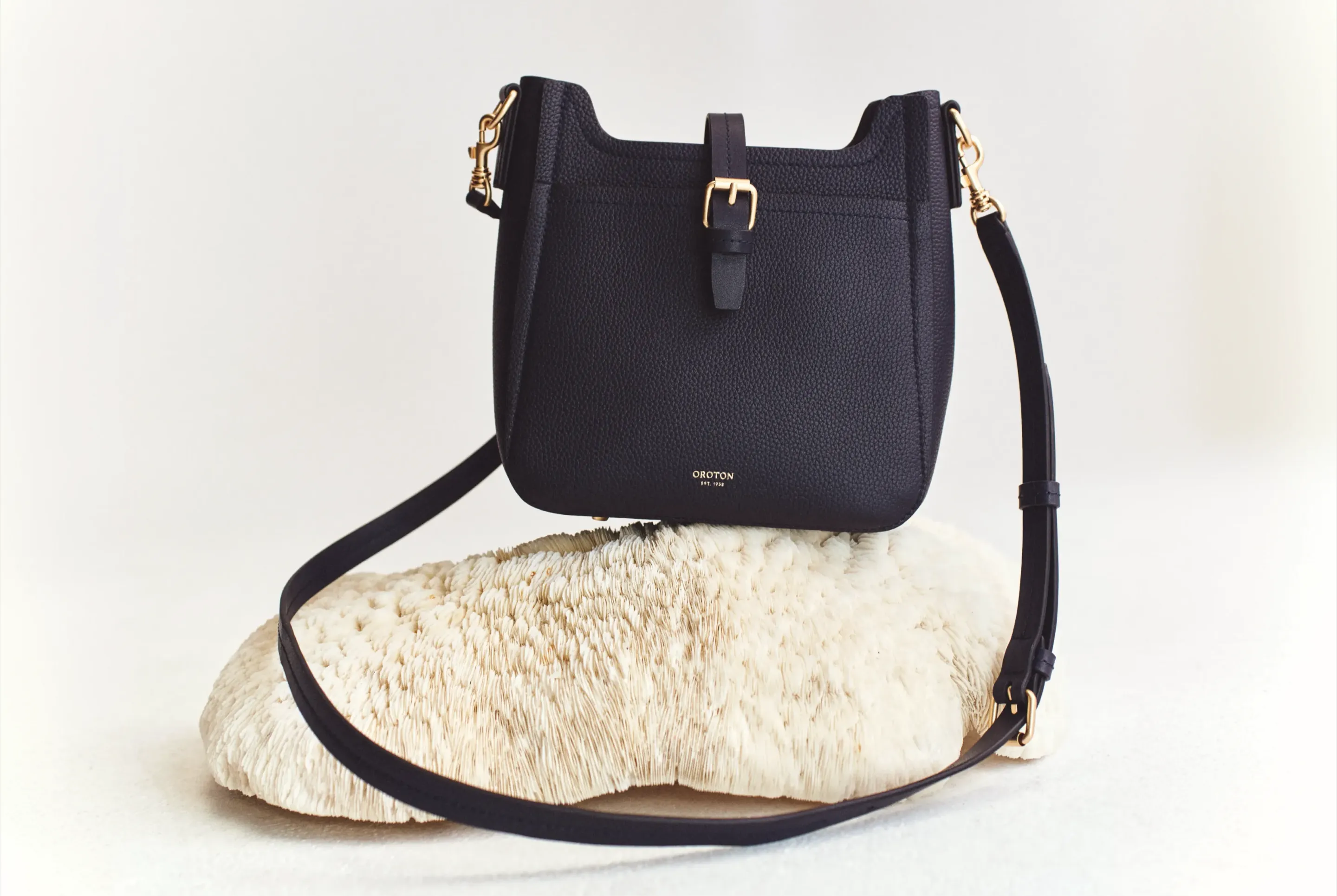 A black handbag with a gold buckle resting on a stone.