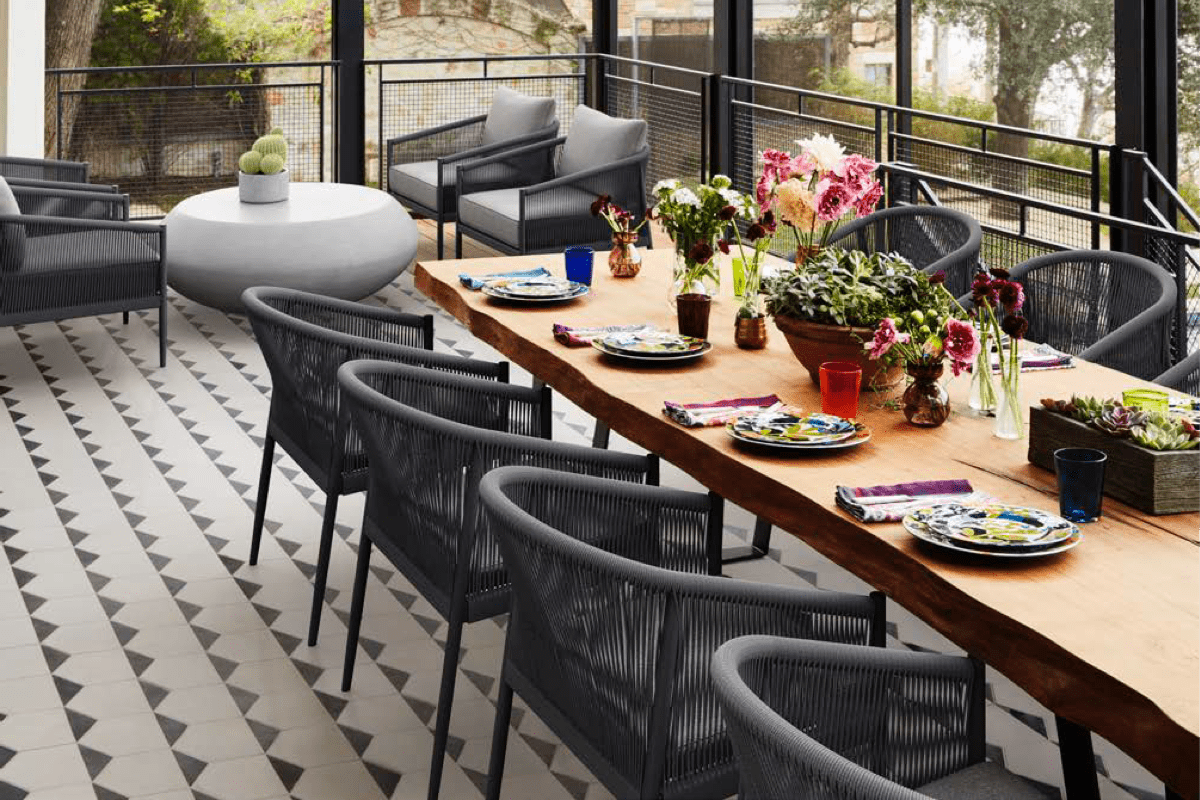 Modern woven black dining chairs around a long wooden table on an outdoor deck with black and white checkered tiles.