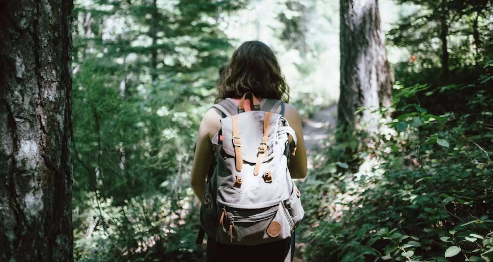 a woman walks in the woods with a gray backpack