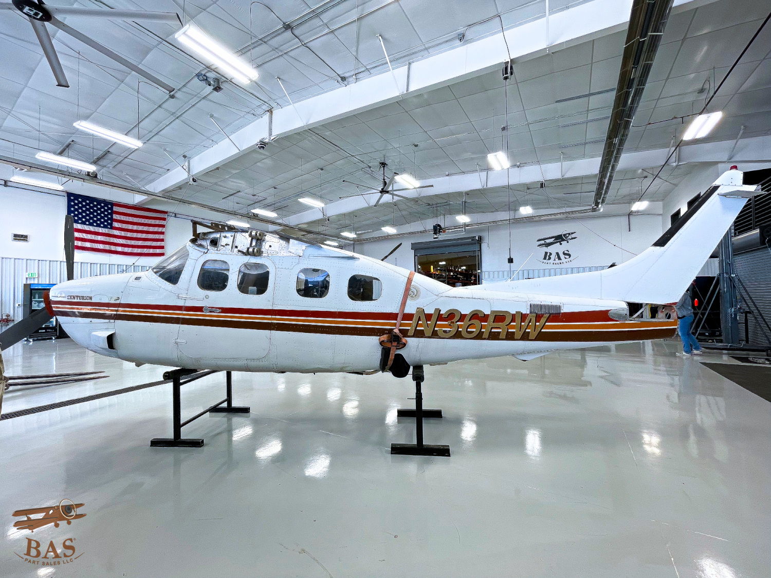 Small aircraft inside a hangar with an American flag in the background.