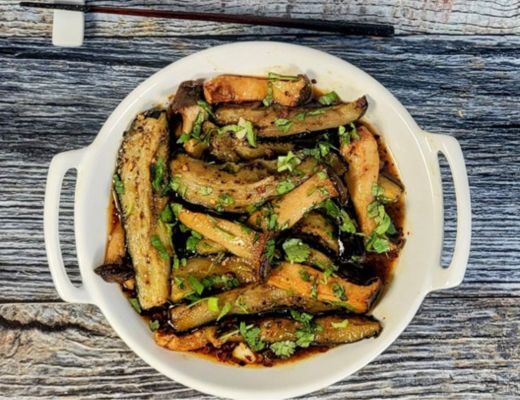 Bowl of cooked green vegetables garnished with herbs on a wooden surface.
