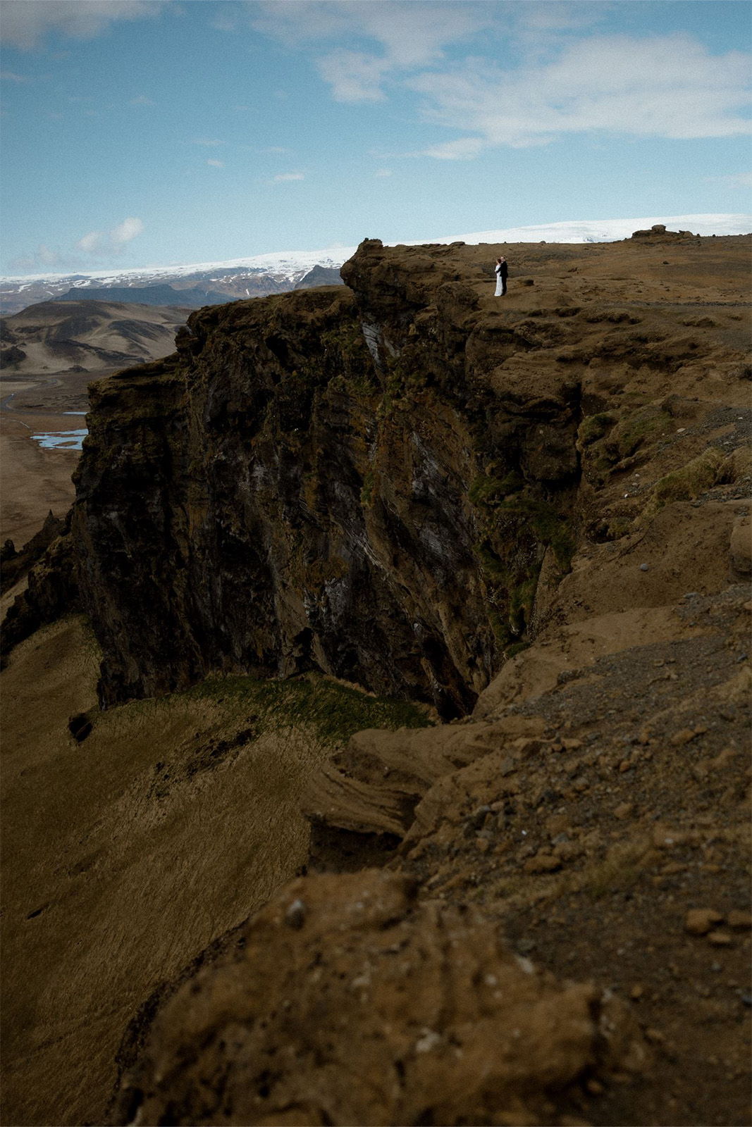 Person standing on a cliff overlooking a vast landscape under a blue sky.