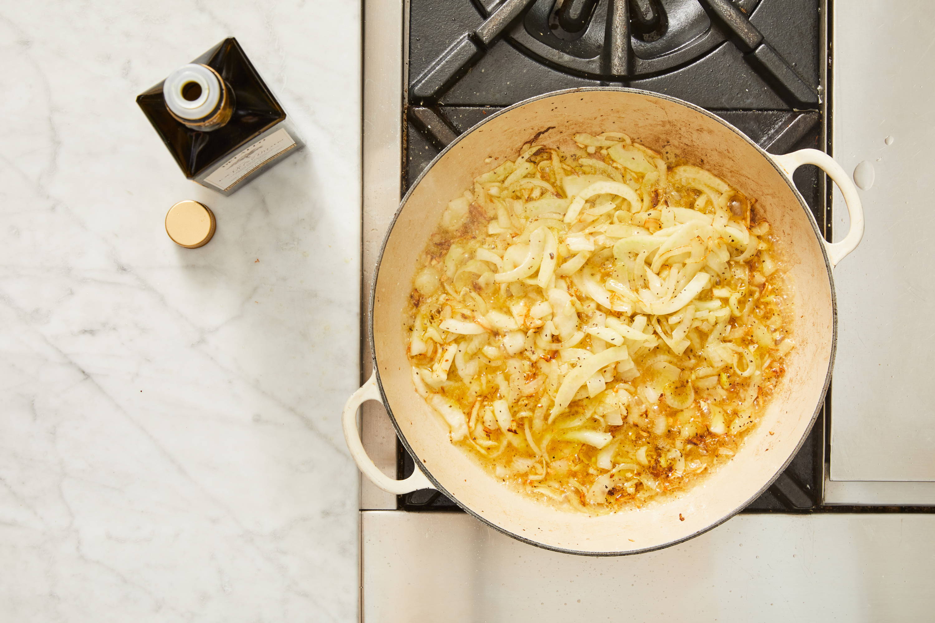 Pot with oil, onion, fennel, garlic, salt, and pepper cooking on a stove top.