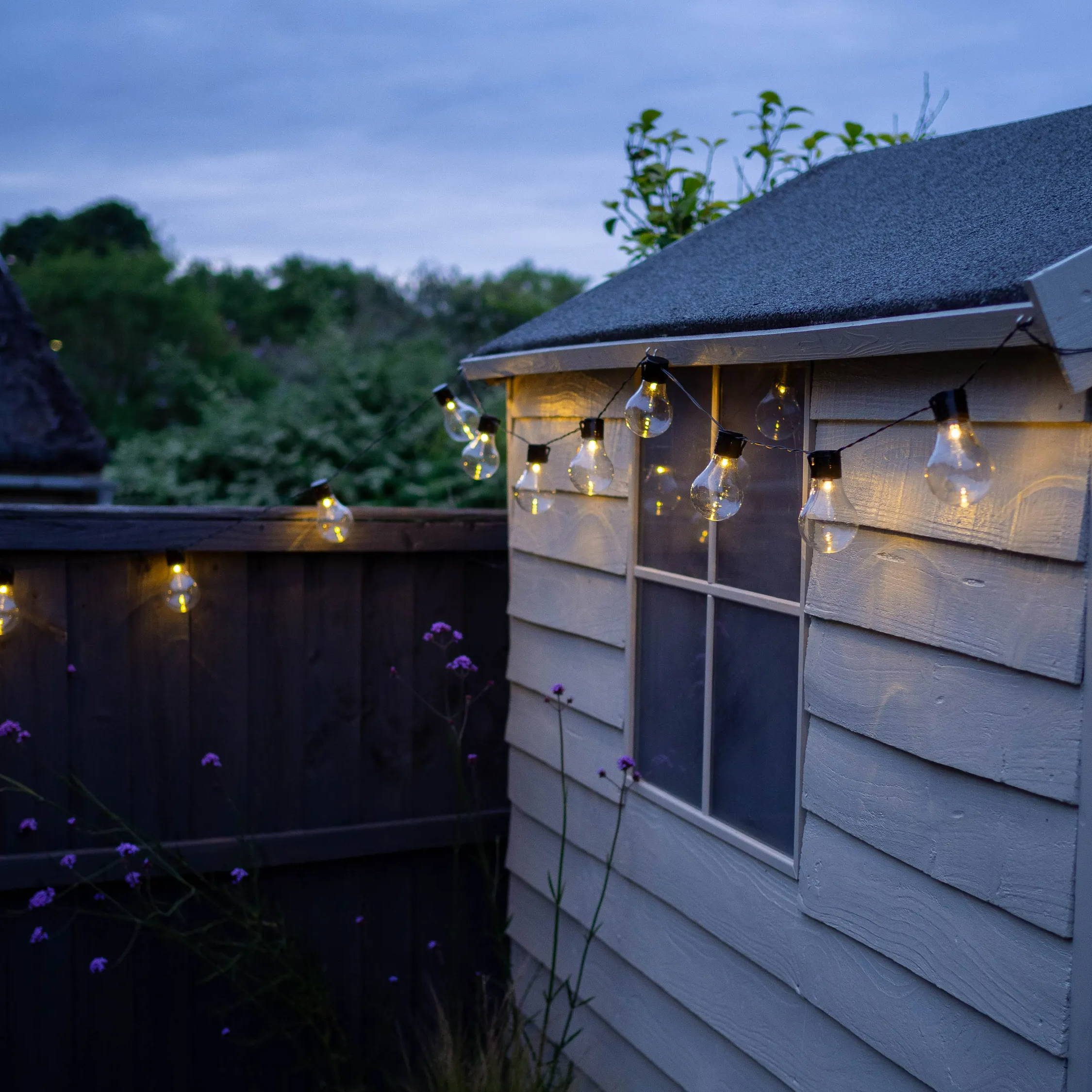 Solar festoon lights on a garden shed at night.