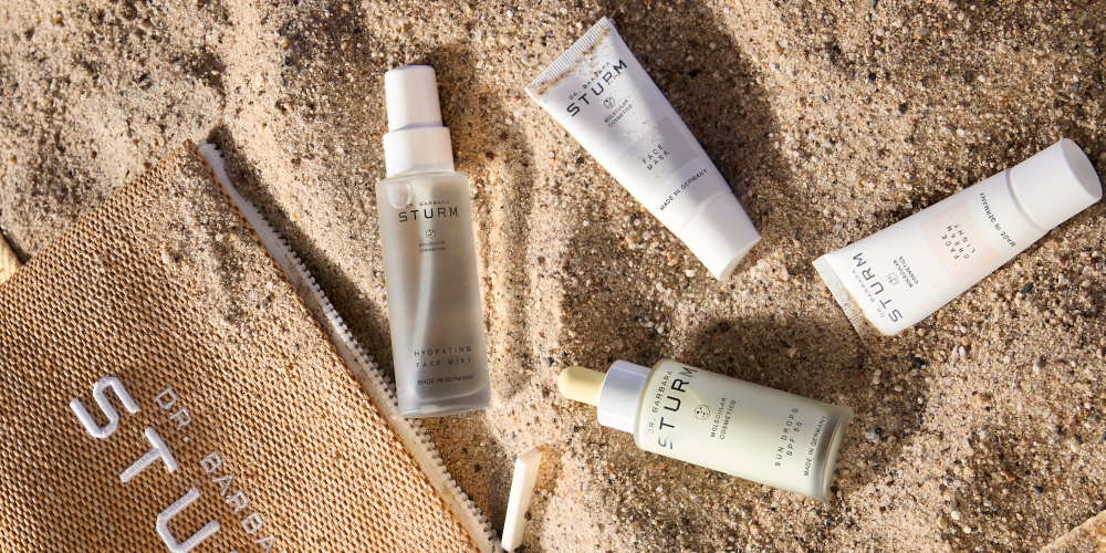 Skincare products placed on sandy surface next to a bag.