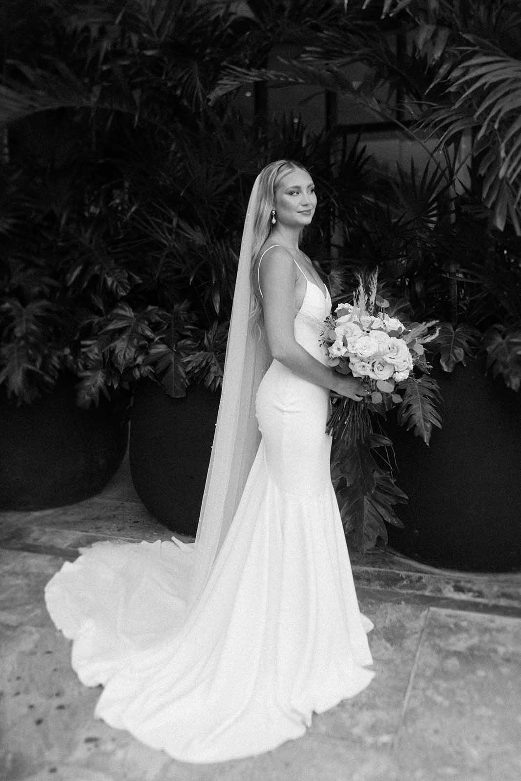 Black and white image of GRACE Bride wearing the Clo Crepe gown and Pearly Long Veil while holding bouquet