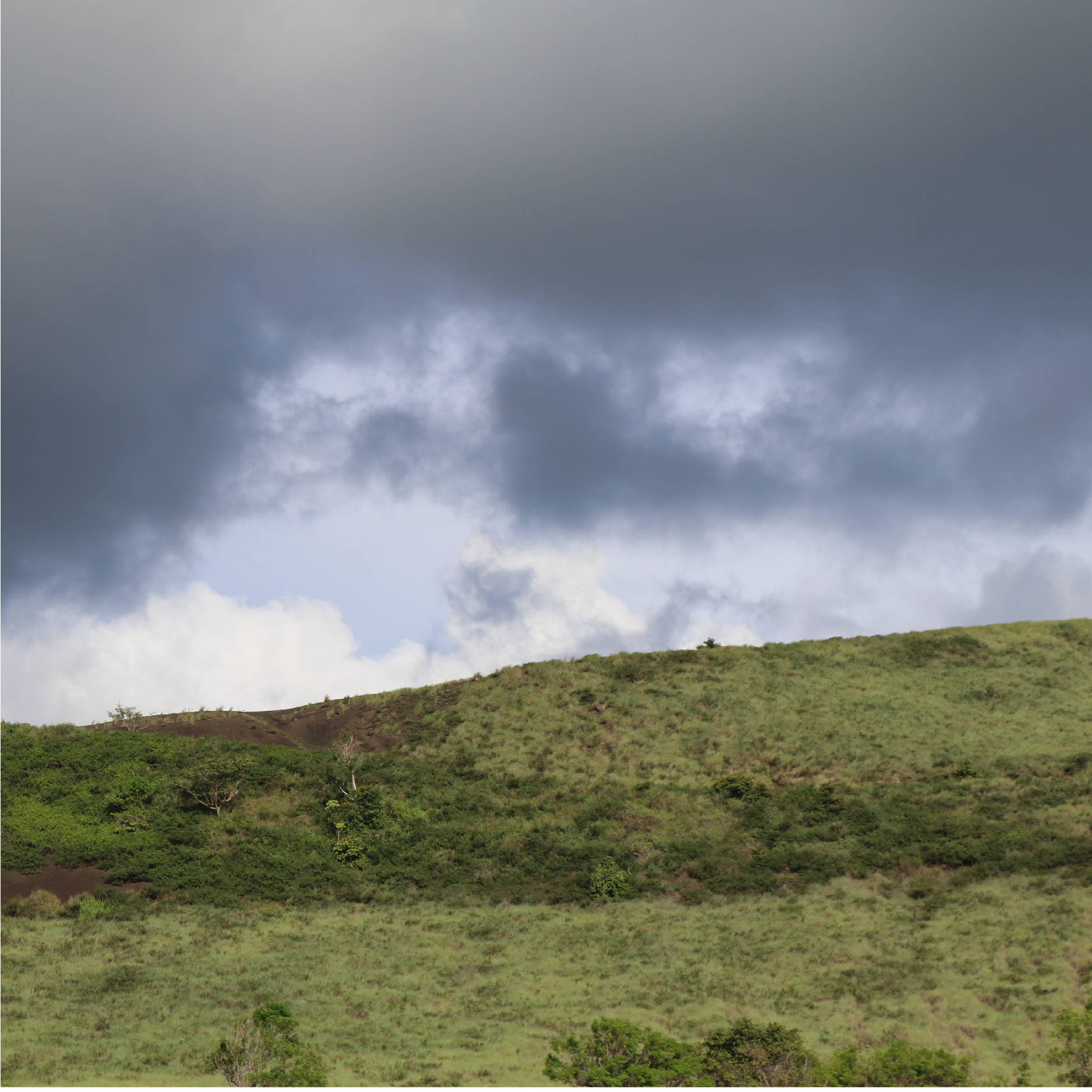 A large green hill in Nicaragua contrasts a dark stormy sky. 