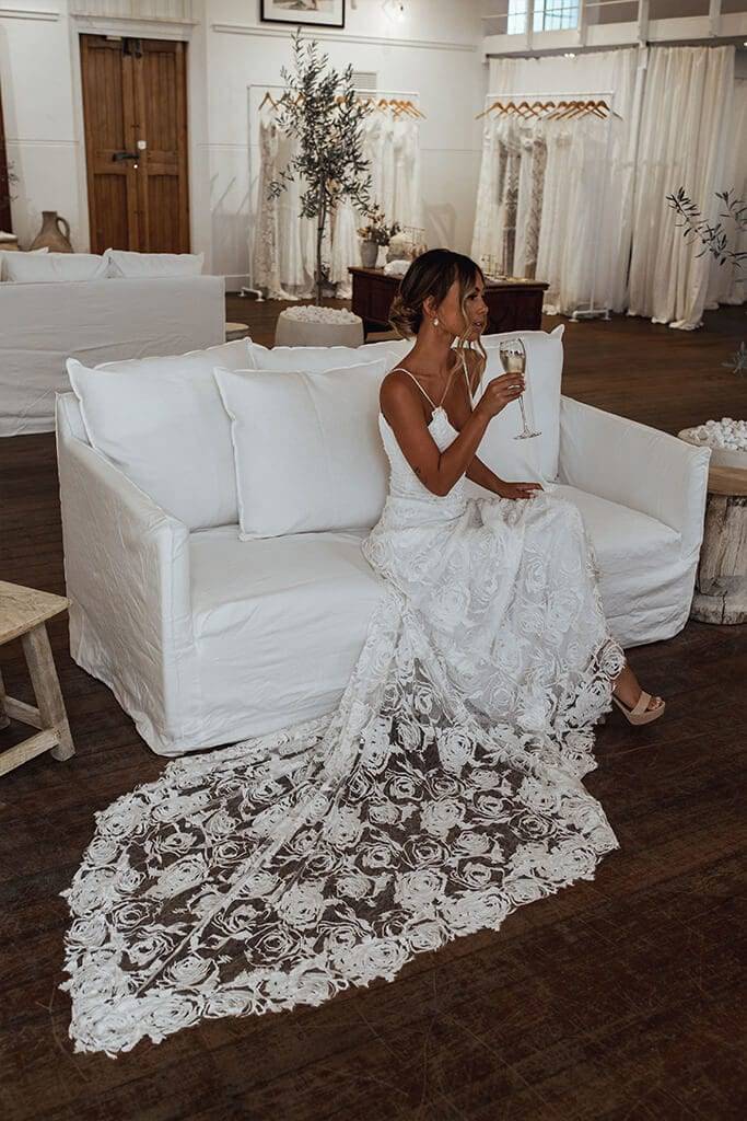 Bride sipping champagne on the white linen couch inside Grace Loves Lace Perth showroom